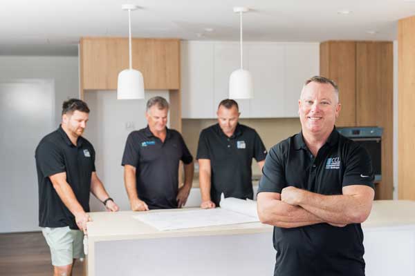 Four of the Coastal Commercial Linings team are in a kitchen. One is smiling at the camera, the others are looking at plans.