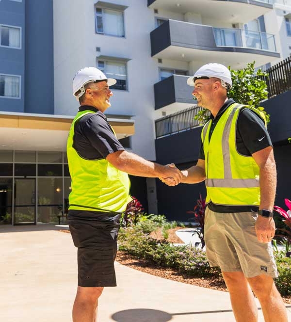 A male plasterer shaking hands with a male builder in front of a commercial apartment building in Port Macquarie.